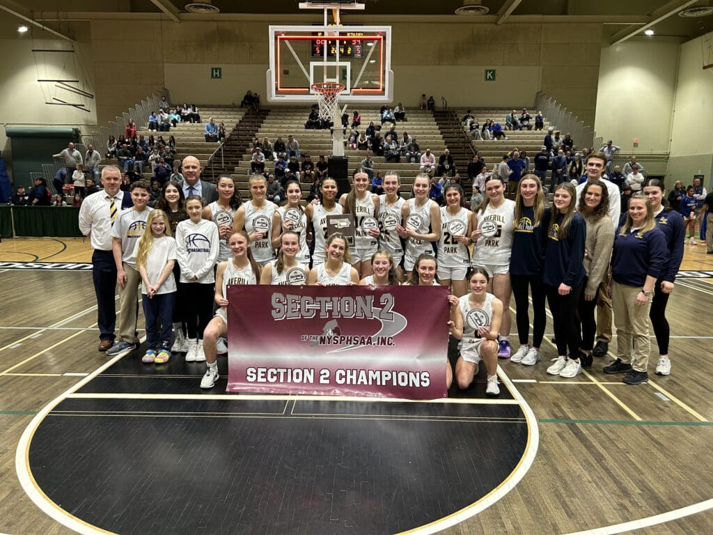 The girls basketball team poses for a photo with a banner after their win.